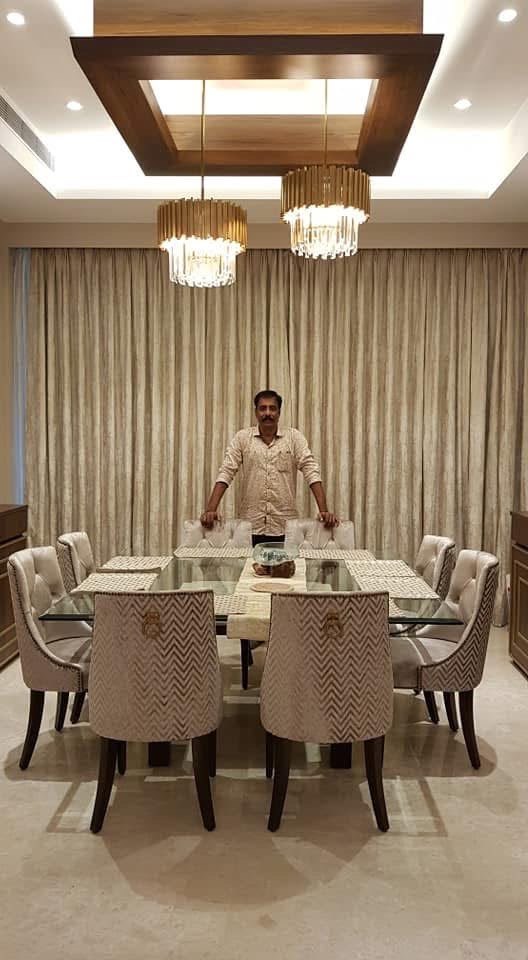 A man standing at a dining table in a finished dining room with gold curtains and chandeliers, from a Laxmi Decorz project